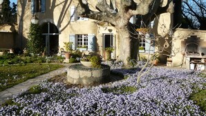 Un edificio tradicional con un jardín delantero, que presenta un gran árbol y flores en flor.