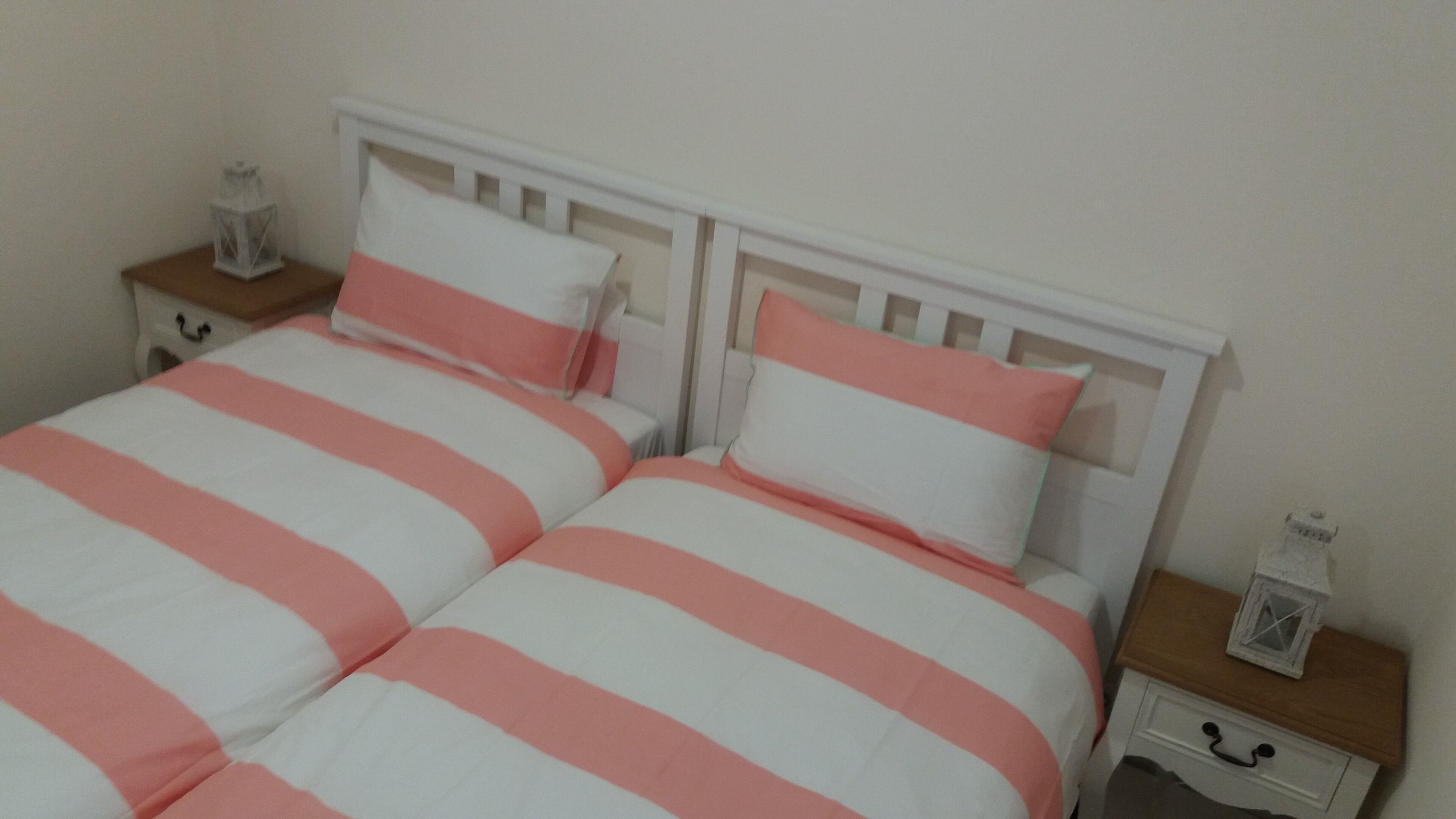 A double bed with pink and white striped bedding, a white headboard, and two bedside tables with white lanterns.