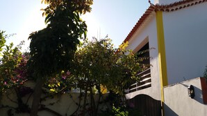 A building with a yellow vertical stripe, a red-tiled roof, and a window with a metal gate. - Quinta da princesa Barbara (Caldas da Rainha)