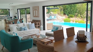 Un ampio soggiorno con un grande tavolo da pranzo, posti a sedere confortevoli e vista su una piscina e un giardino.