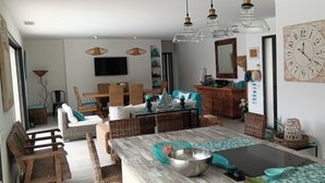 Un soggiorno moderno con zona pranzo, mobili in vimini, un grande specchio e un orologio a parete.