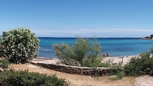 Vista costiera con spiaggia sabbiosa, alcune persone e barche in acqua.
