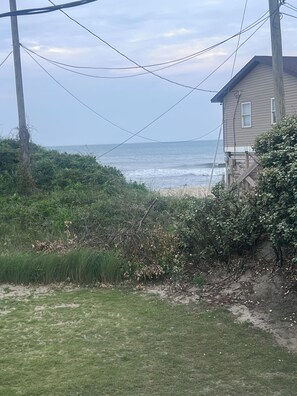A coastal view with a house, power lines, and vegetation. - Lovely 3 Bedroom Oceanside Cottage With No Street To Cross. (Nags Head)