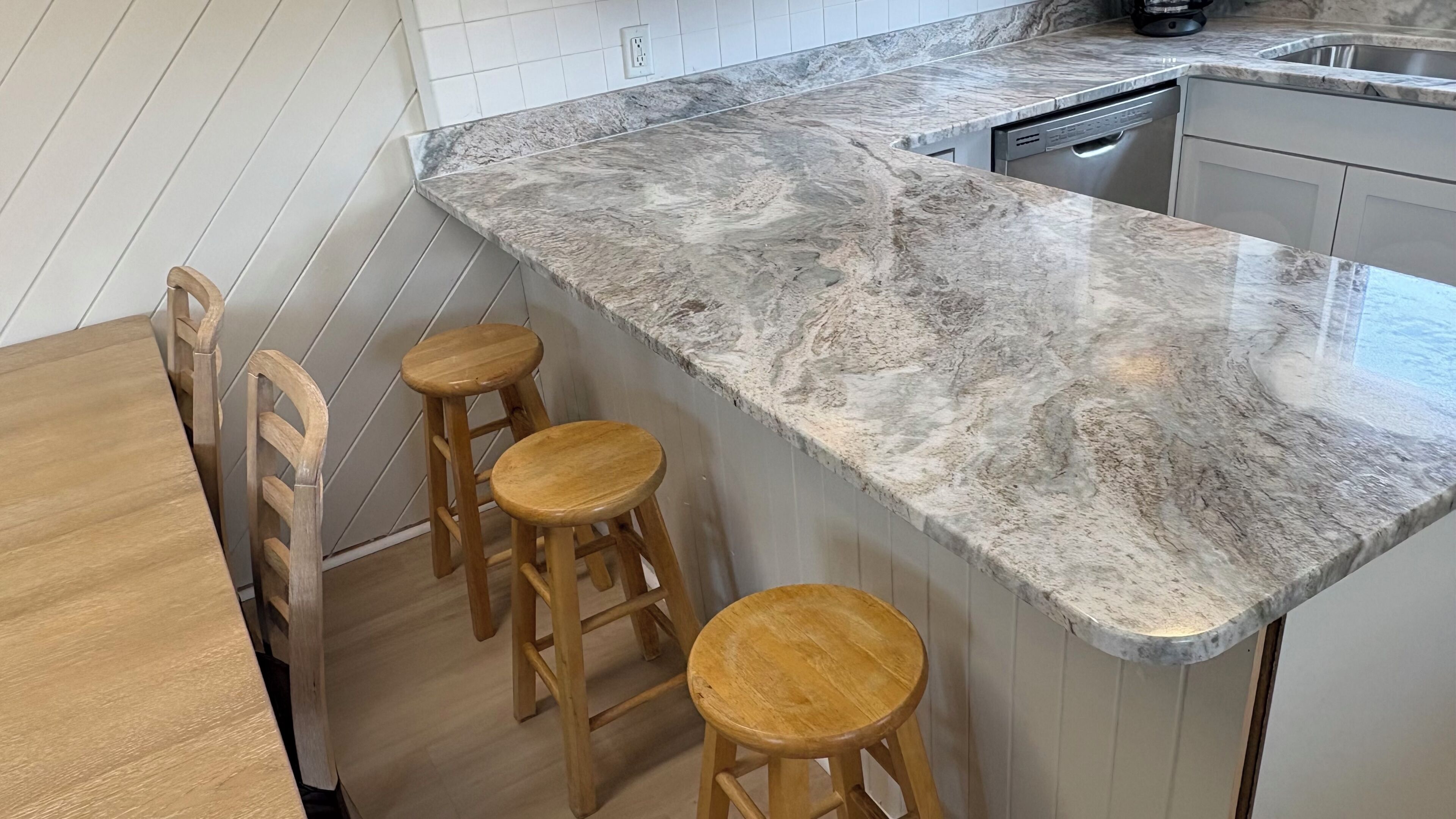 A kitchen with a marble countertop, wooden stools, and a dishwasher.