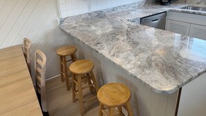 Una cocina con encimera de mármol, taburetes de madera y lavavajillas.