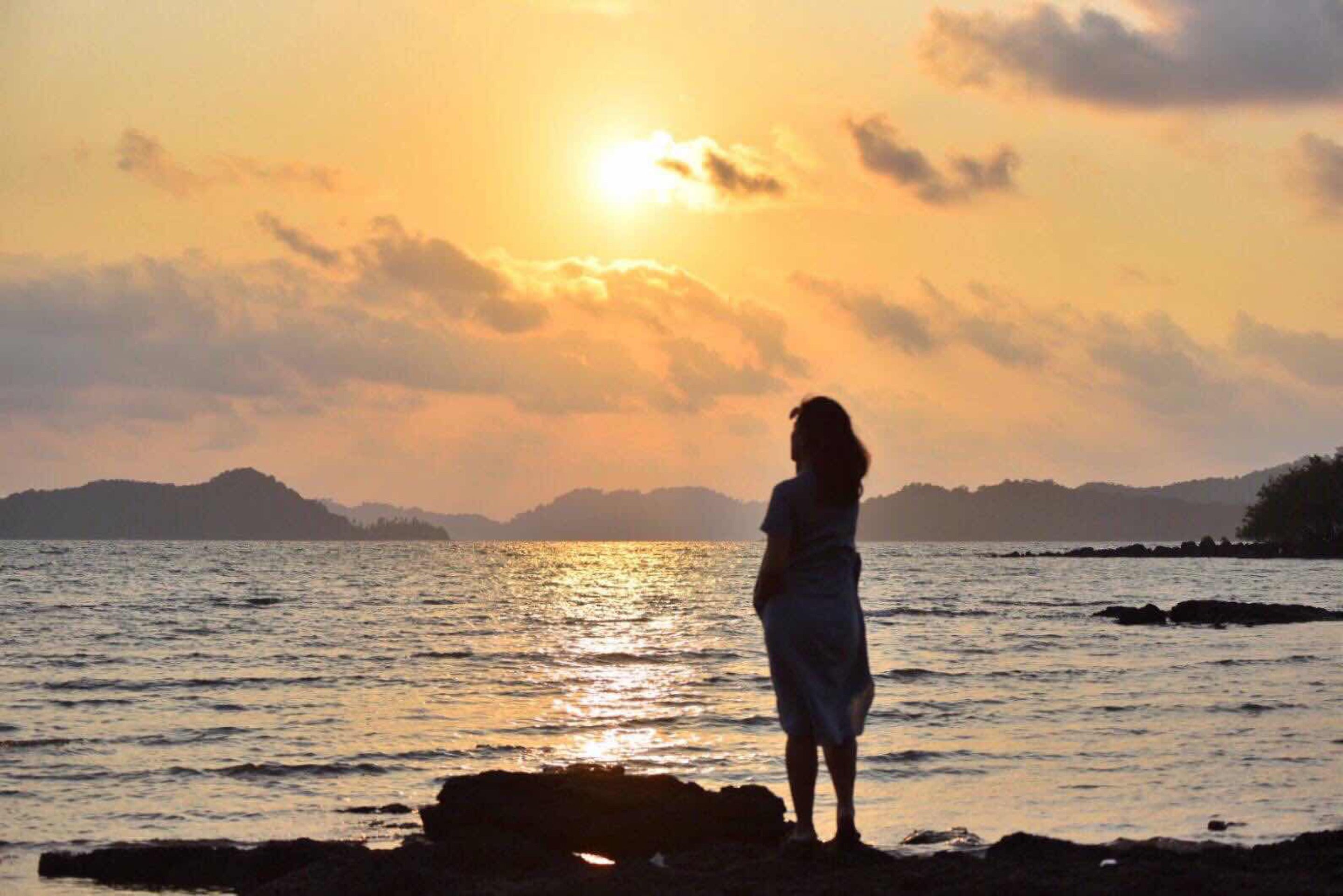 Una persona de pie junto a un cuerpo de agua al atardecer.
