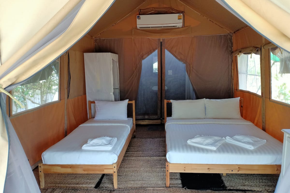 Une tente équipée de deux lits, d’un appareil de climatisation et offrant une vue sur l’extérieur.