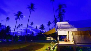 A tented accommodation with a view of palm trees at night.