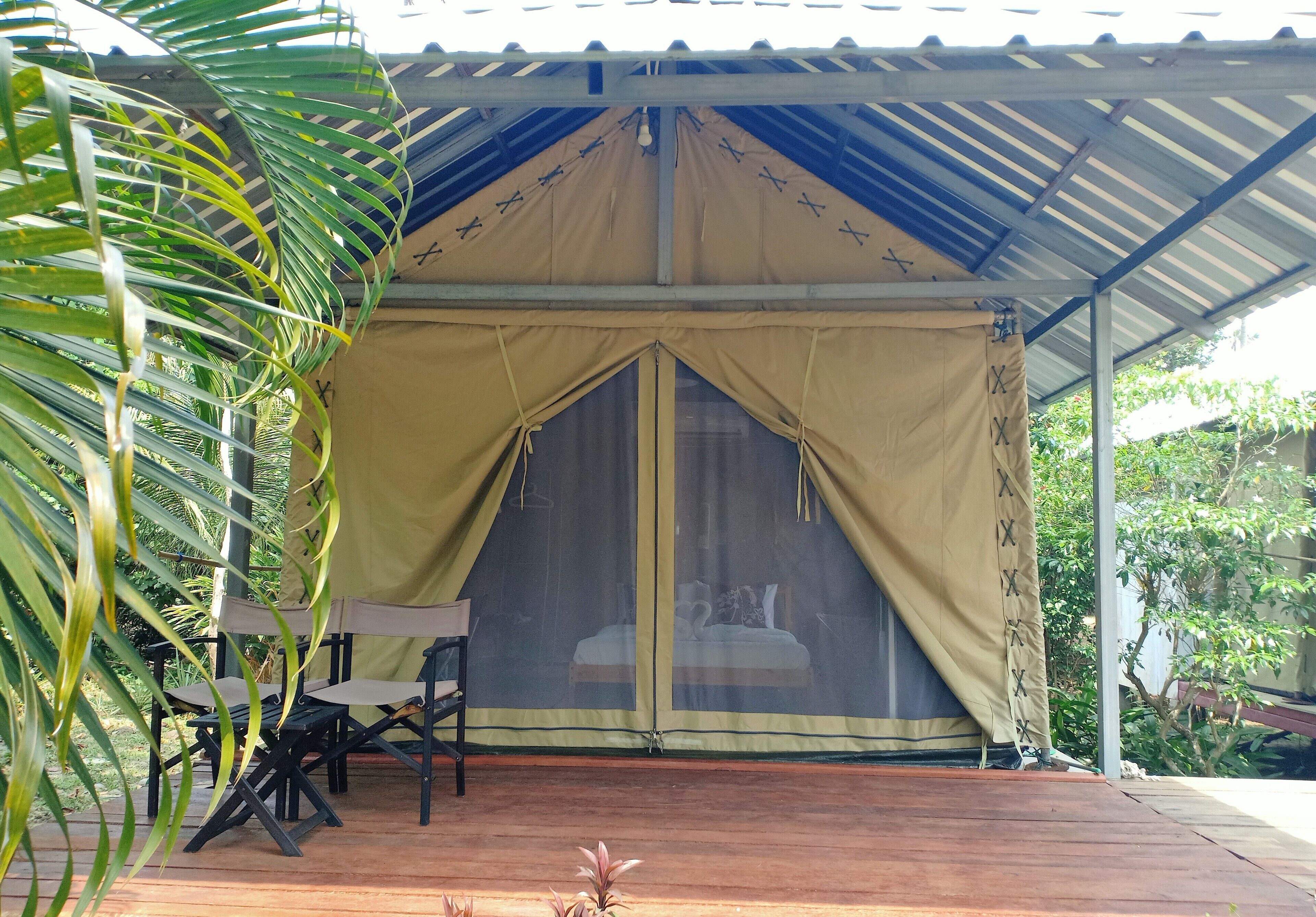 Une structure en forme de tente abritant un lit, entourée de chaises et dotée d’une terrasse en bois.