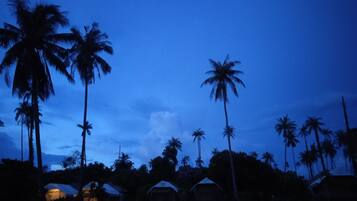 Un resort tropical con palmeras y cabañas de techo de paja bajo un cielo crepuscular.