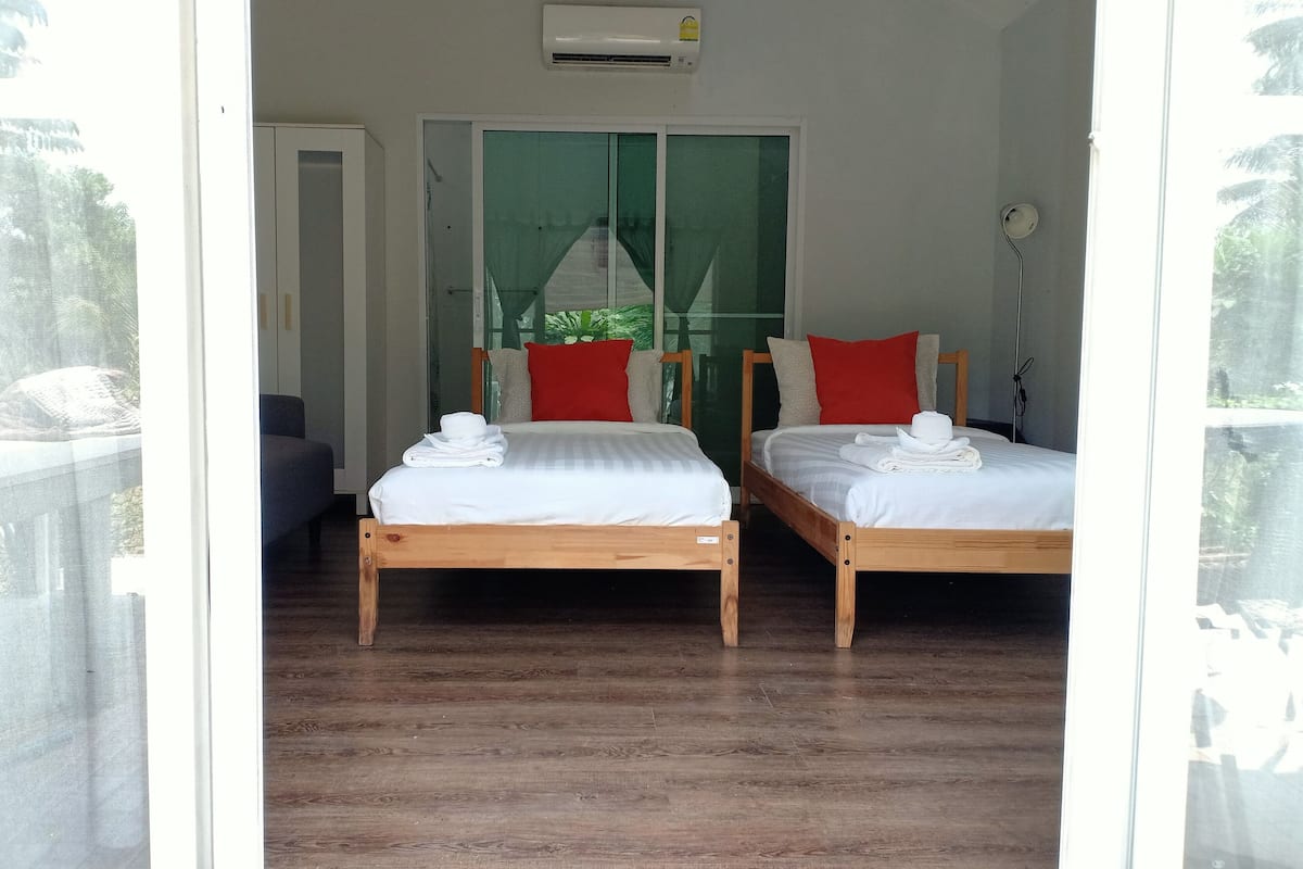 Une chambre avec deux lits en bois, du linge de lit blanc, des oreillers rouges et une serviette blanche sur chaque lit.