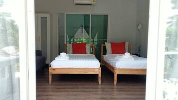 A room with two wooden beds, white bedding, red pillows, and a white towel on each bed.