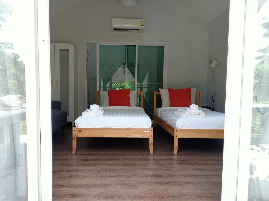 A room with two wooden beds, white bedding, red pillows, and a white towel on each bed.