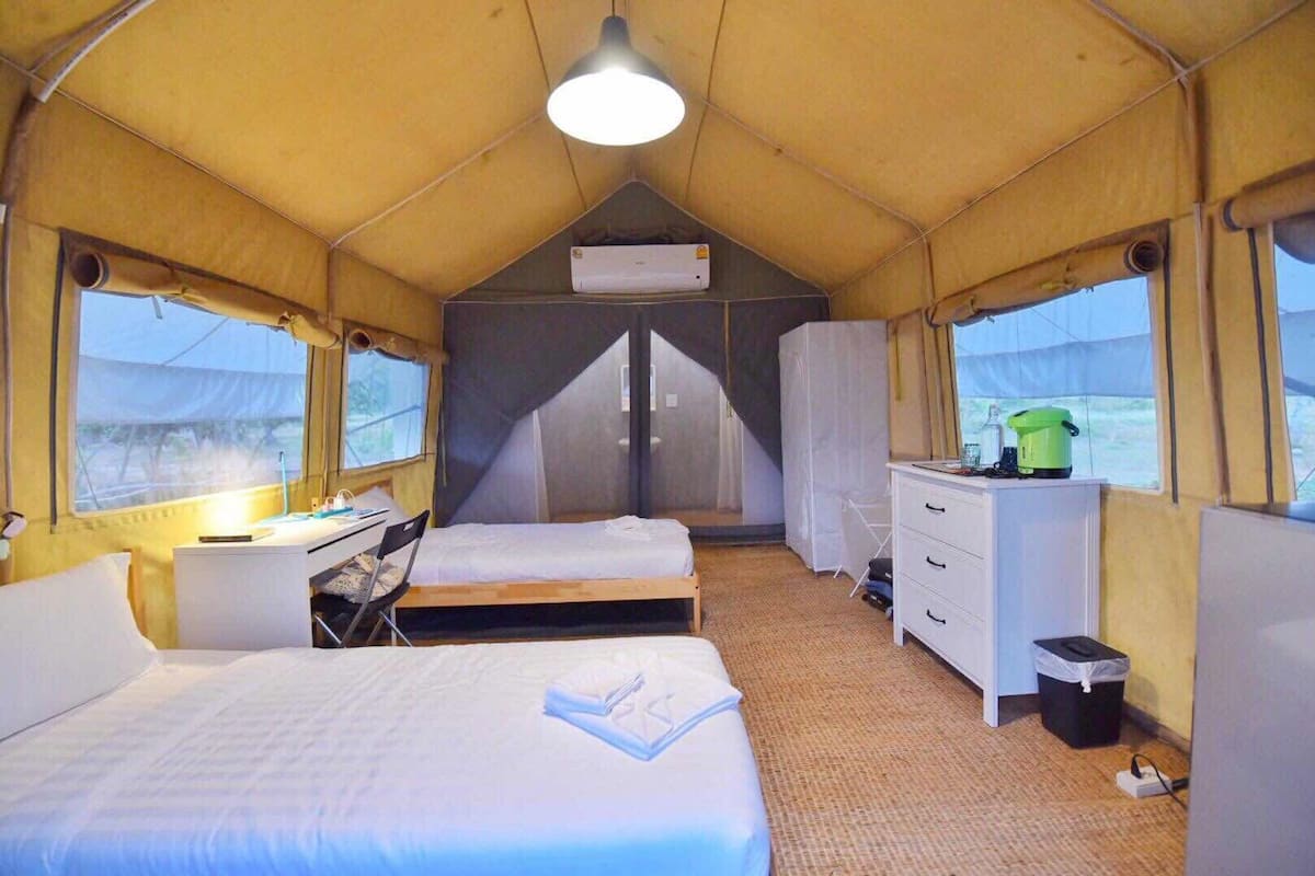 Une pièce aménagée comme une tente, avec deux lits, un bureau, une commode et une fenêtre.