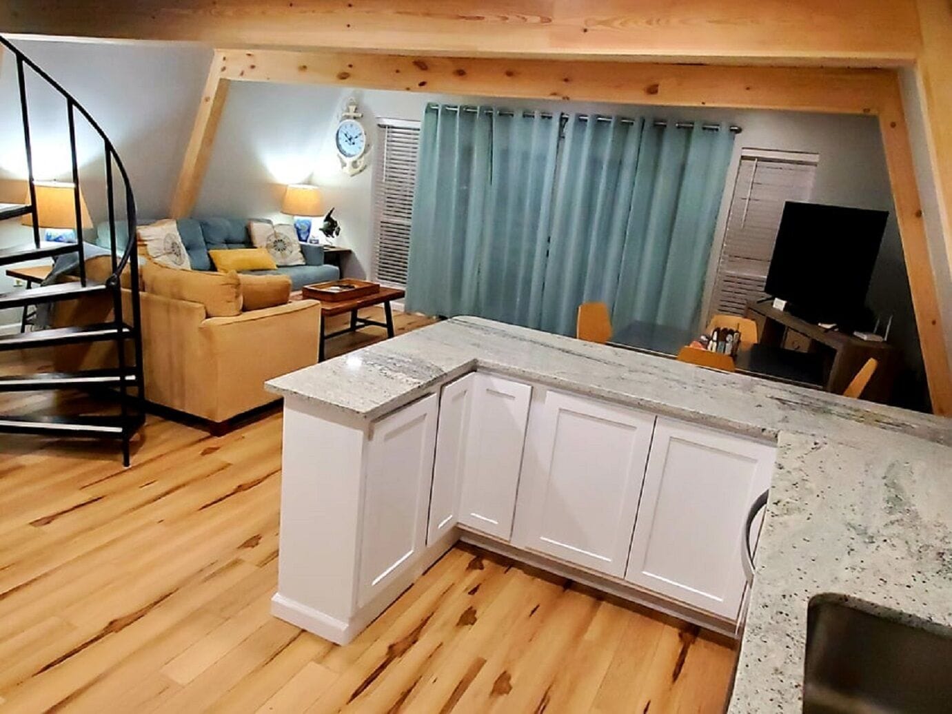 Un salon chaleureux avec un îlot de cuisine, un plancher en bois et un rideau bleu.