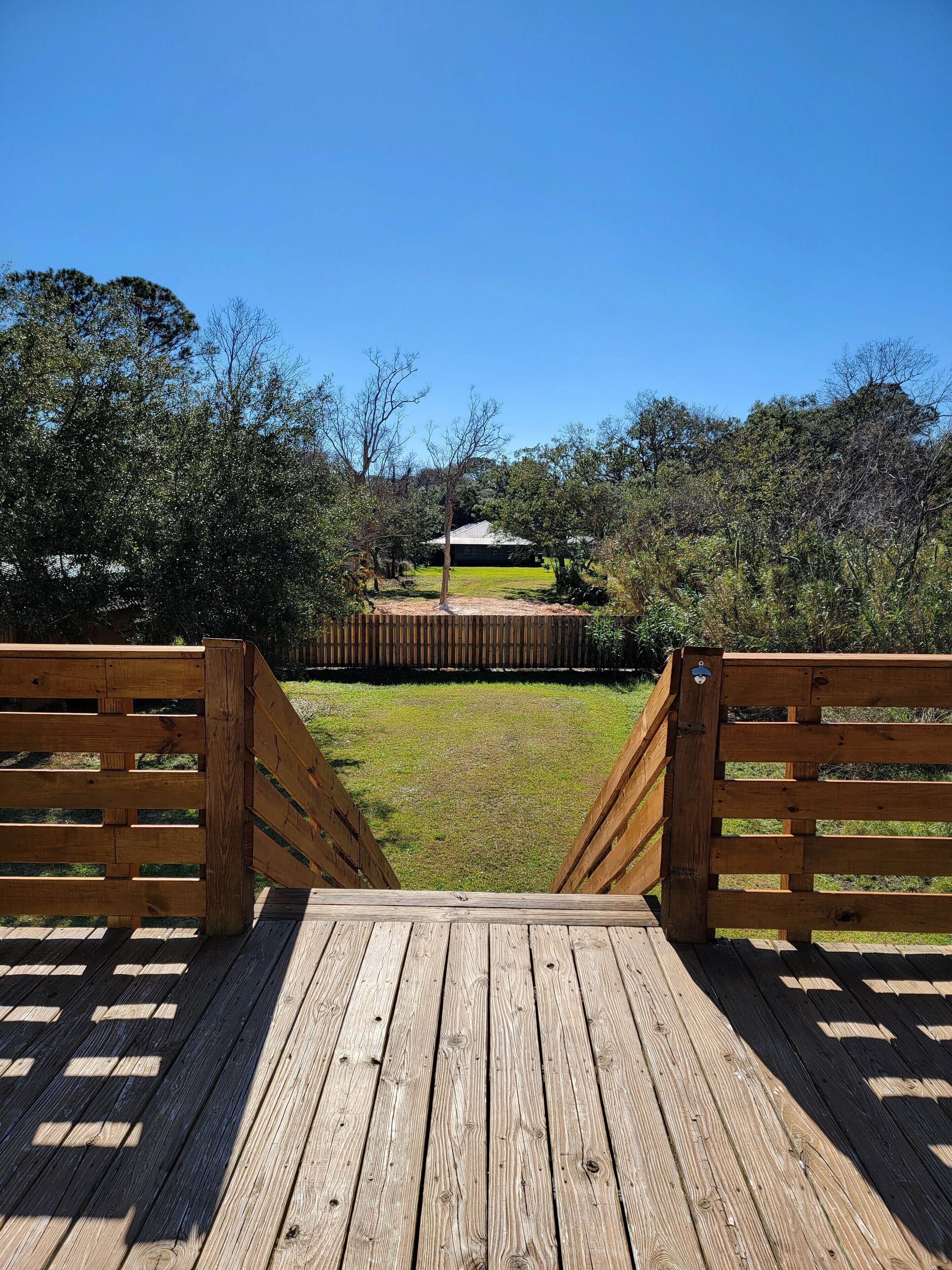 A wooden deck leading to a grassy area with a building in the background.