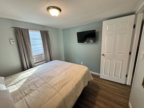 A bedroom with a bed, a TV mounted on the wall, a door, and a window with curtains. - Pet Friendly | Walk to Lake | Firepit & Grill (Geneva)