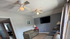 Un salon spacieux doté d’un plancher en bois, de deux canapés, d’un téléviseur et de ventilateurs de plafond.