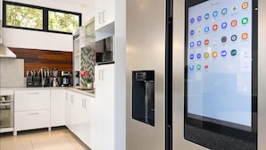 Una cocina moderna con armarios blancos, horno empotrado, cafetera y una pantalla grande mostrando iconos de aplicaciones.