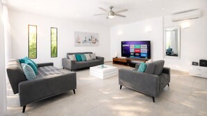 Una sala de estar moderna con dos sofás grises, una mesa de centro blanca y un televisor de pantalla plana que muestra servicios de transmisión.