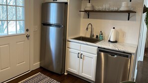 A modern kitchen with white cabinetry, stainless steel appliances, a built-in dishwasher, and a window with a view of trees. - A Great Apartment In The Middle Of It All! (Nashville)