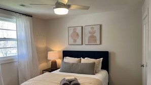 A bedroom with a bed, a ceiling fan, a nightstand with a lamp, and two wall-mounted artworks. - A Great Apartment In The Middle Of It All! (Nashville)