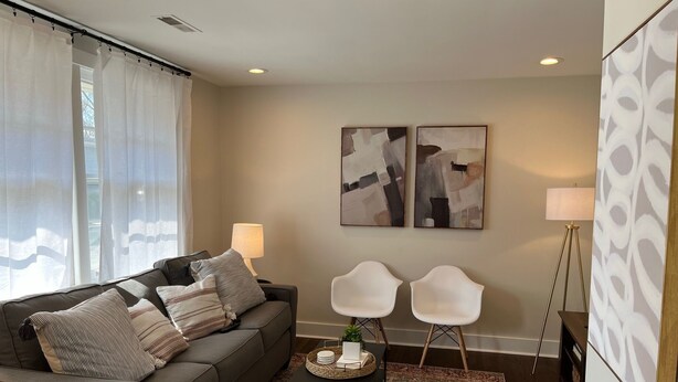A modern living room with a grey sofa, two white chairs, a patterned rug, and abstract art on the walls. - A Great Apartment In The Middle Of It All! (Nashville)