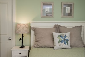 Un dormitorio con una cama, dos mesitas de noche, una lámpara y dos cuadros en la pared.