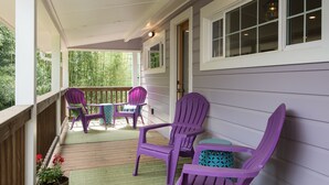 Une véranda avec des balustrades en bois, un tapis vert et des fauteuils Adirondack violets.