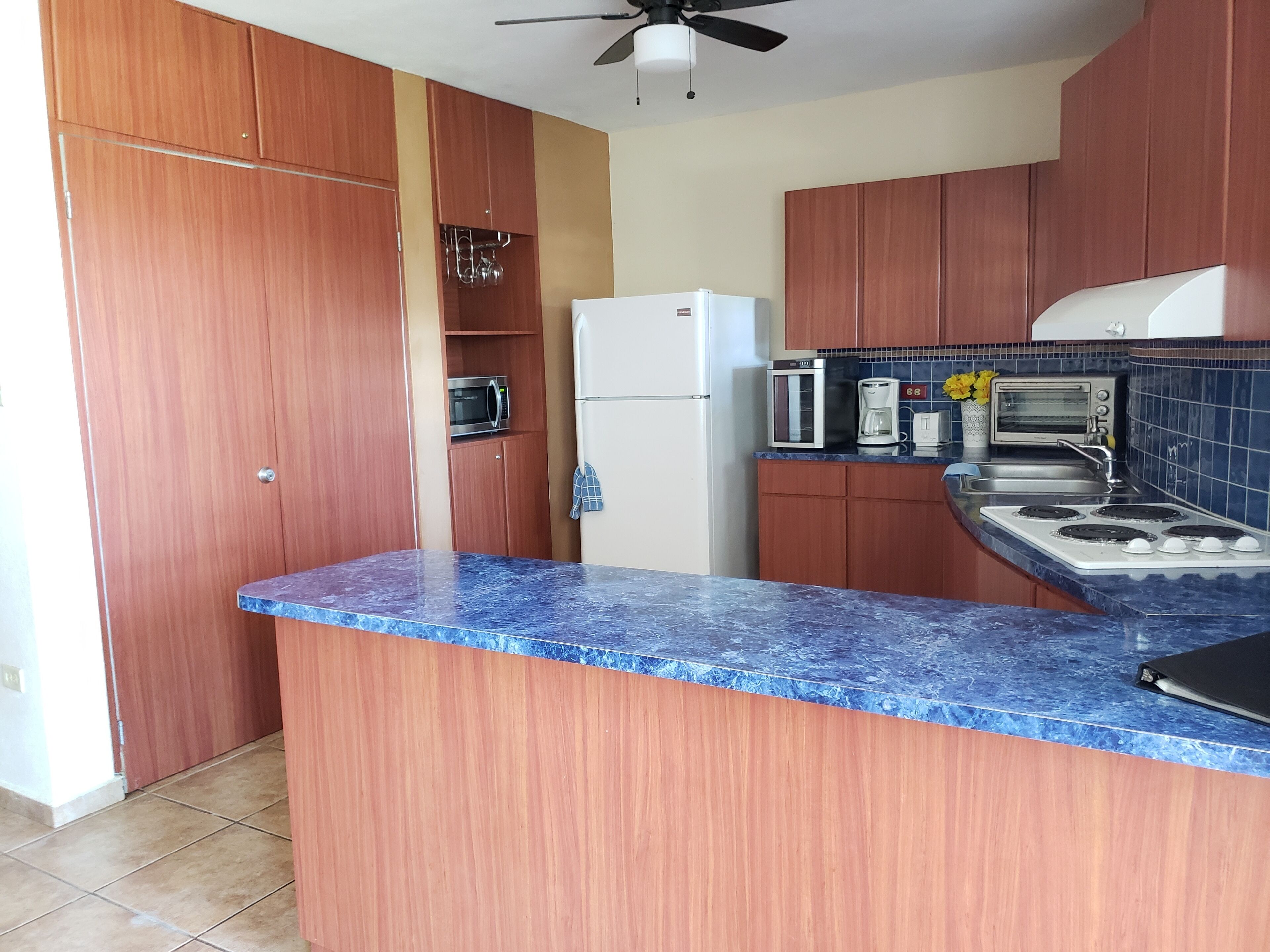 Une cuisine avec des meubles en bois, un plan de travail en marbre bleu, un réfrigérateur blanc, un four à micro-ondes, un grille-pain et une cuisinière.