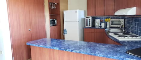 Une cuisine avec des meubles en bois, un plan de travail en marbre bleu, un réfrigérateur blanc, un four à micro-ondes, un grille-pain et une cuisinière.