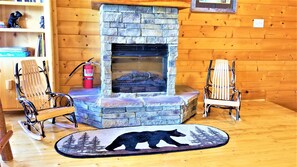 A cozy room with a stone fireplace, two rocking chairs, a rug with a bear design, and a bookshelf with books and figurines.