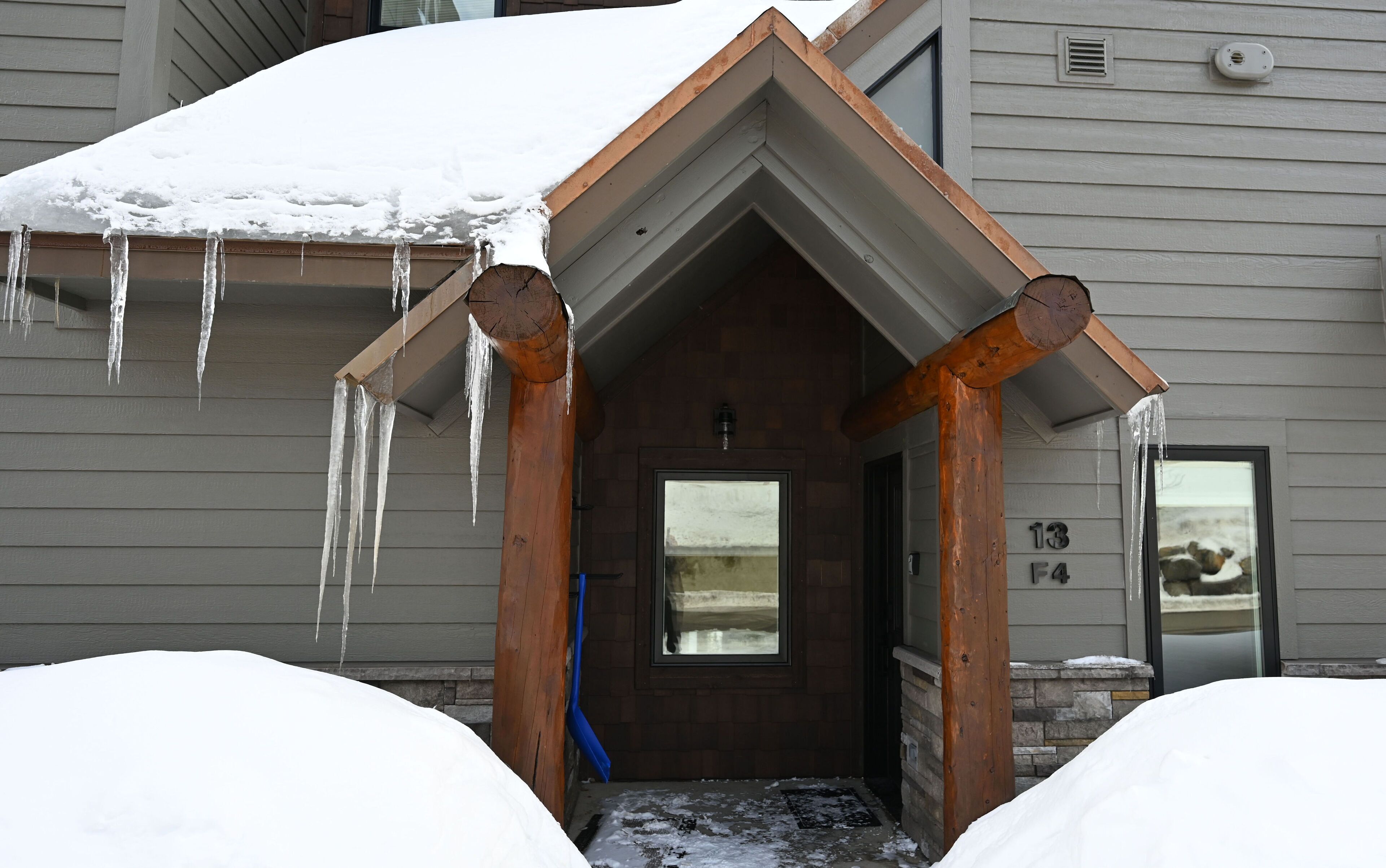 A snow-covered entrance with icicles hanging from the roof, a wooden door, and a stone wall.