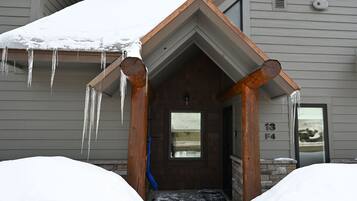 A snow-covered entrance with icicles hanging from the roof, a wooden door, and a stone wall.