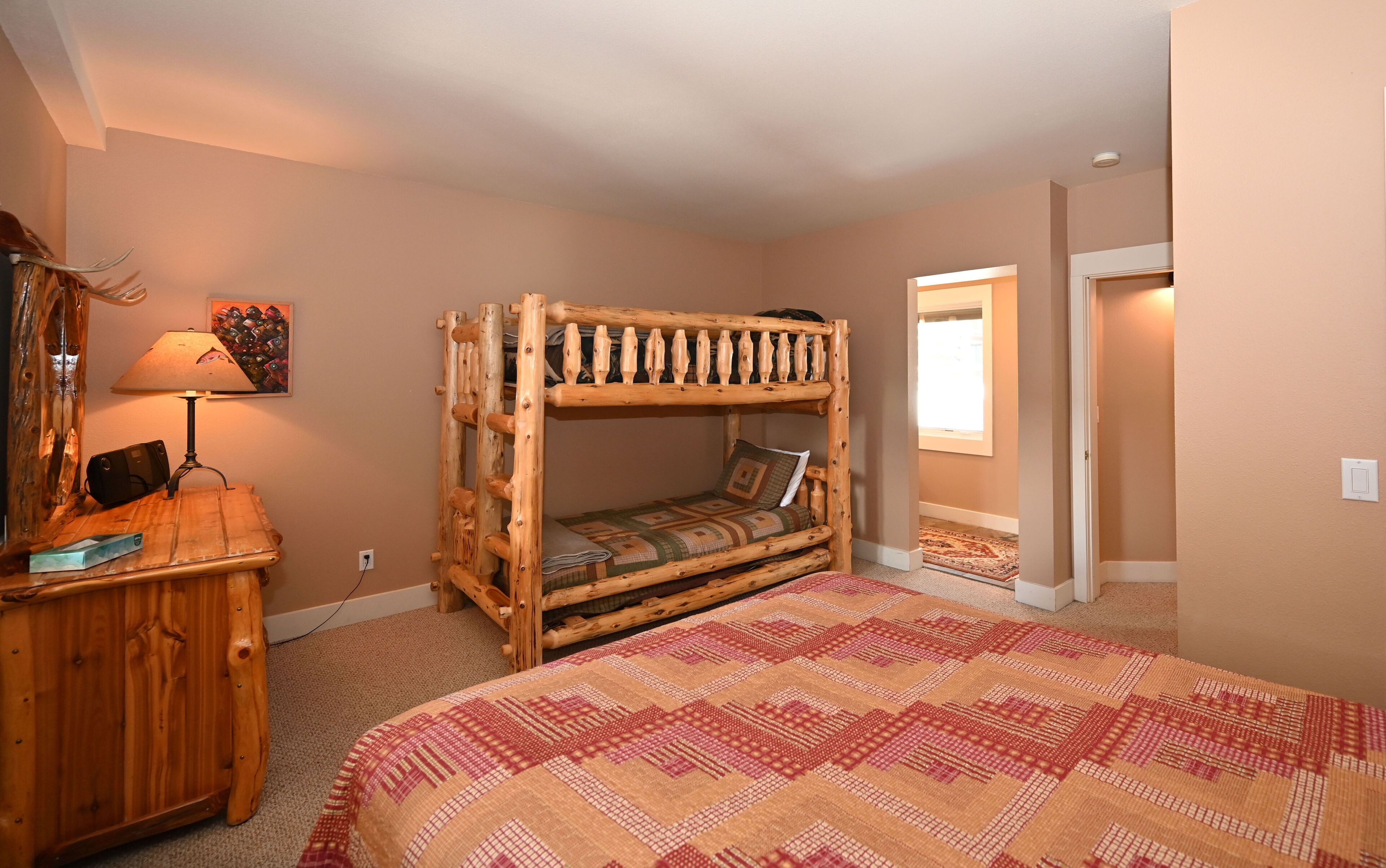 A bunk bed with a patterned bedspread, a wooden nightstand with a lamp, and a painting on the wall.