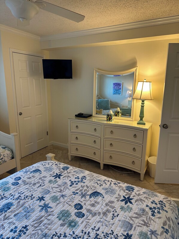 Une chambre à coucher avec un lit, une commode, un miroir et un ventilateur de plafond.