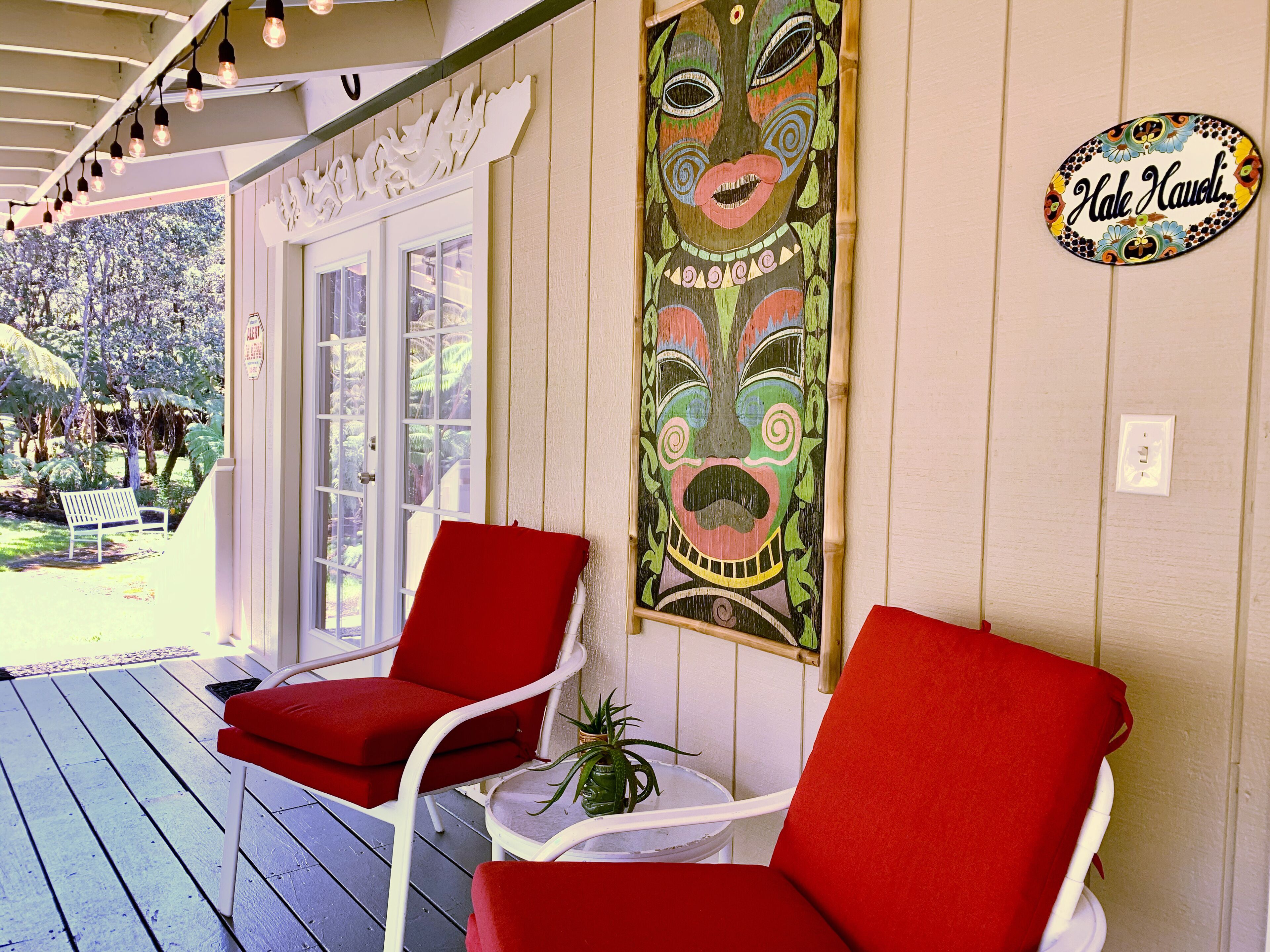 A porch with two red chairs, a wooden table, and a decorative mask on the wall.