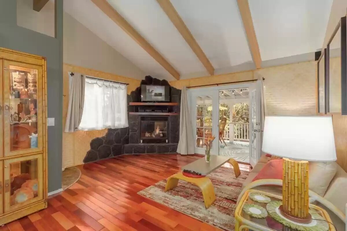 A living room with a fireplace, wooden flooring, a television, and a dining area with a table and chairs.