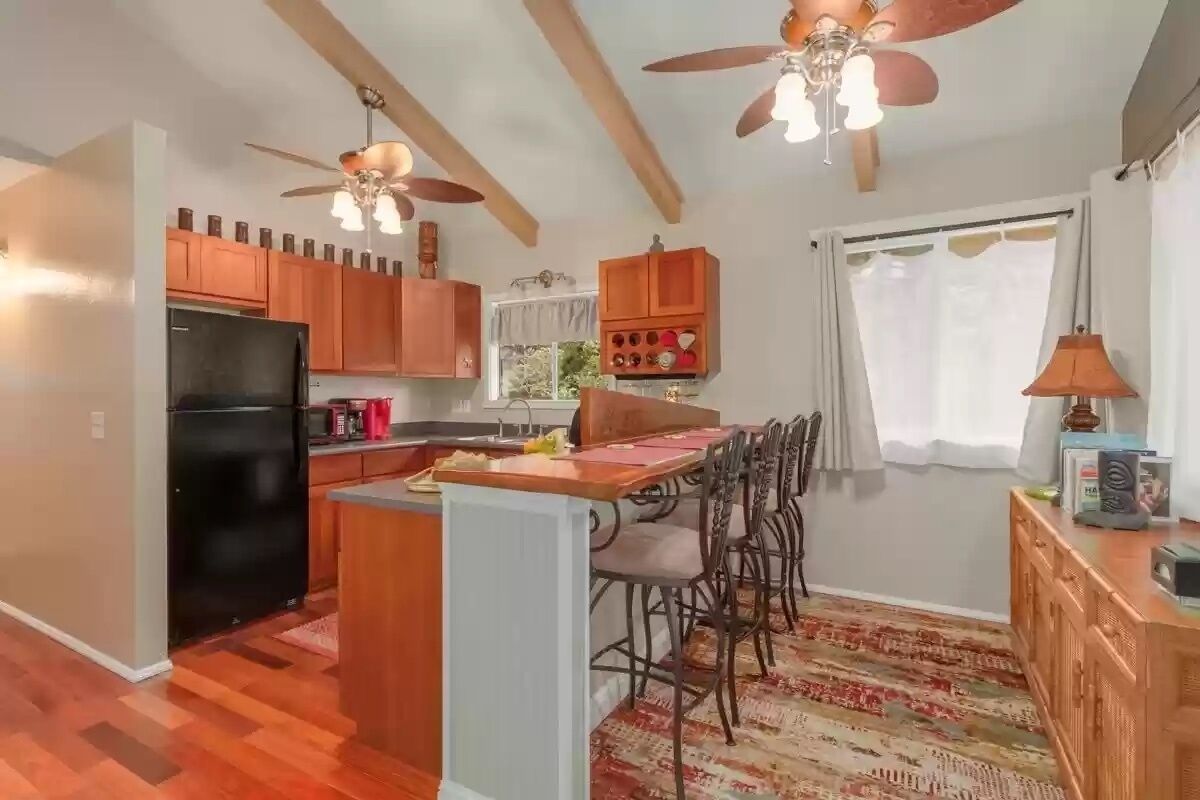 A kitchen with wooden cabinets, a black refrigerator, a dining table with chairs, and a ceiling fan.