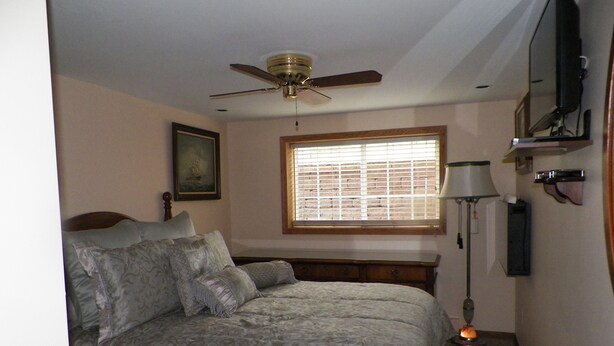 A bedroom with a bed, a ceiling fan, a window with blinds, a bedside lamp, and a framed picture on the wall. - 5 Blocks To The Beach ~ 2 Blocks To Downtown ~ Walk To Everything!   (New Buffalo)