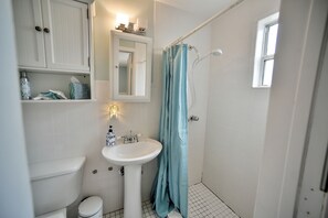 Un baño con inodoro blanco, lavamanos pedestal, espejo y ducha con cortina azul.