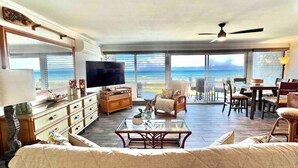 A spacious living room with a large TV, wooden furniture, a glass coffee table, and a view of the ocean. - A jewel on Oceanfront & Breath Taking Views. (Lahaina)