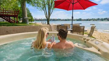 A hot tub with a view of a lake and a red umbrella.