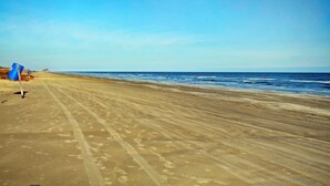 Una spiaggia con cielo sereno, un sentiero sabbioso e alcuni ombrelloni blu.