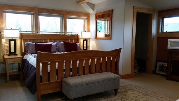 A bedroom with a wooden bed, bedside lamps, a nightstand, a window with blinds, and a door leading to another room.