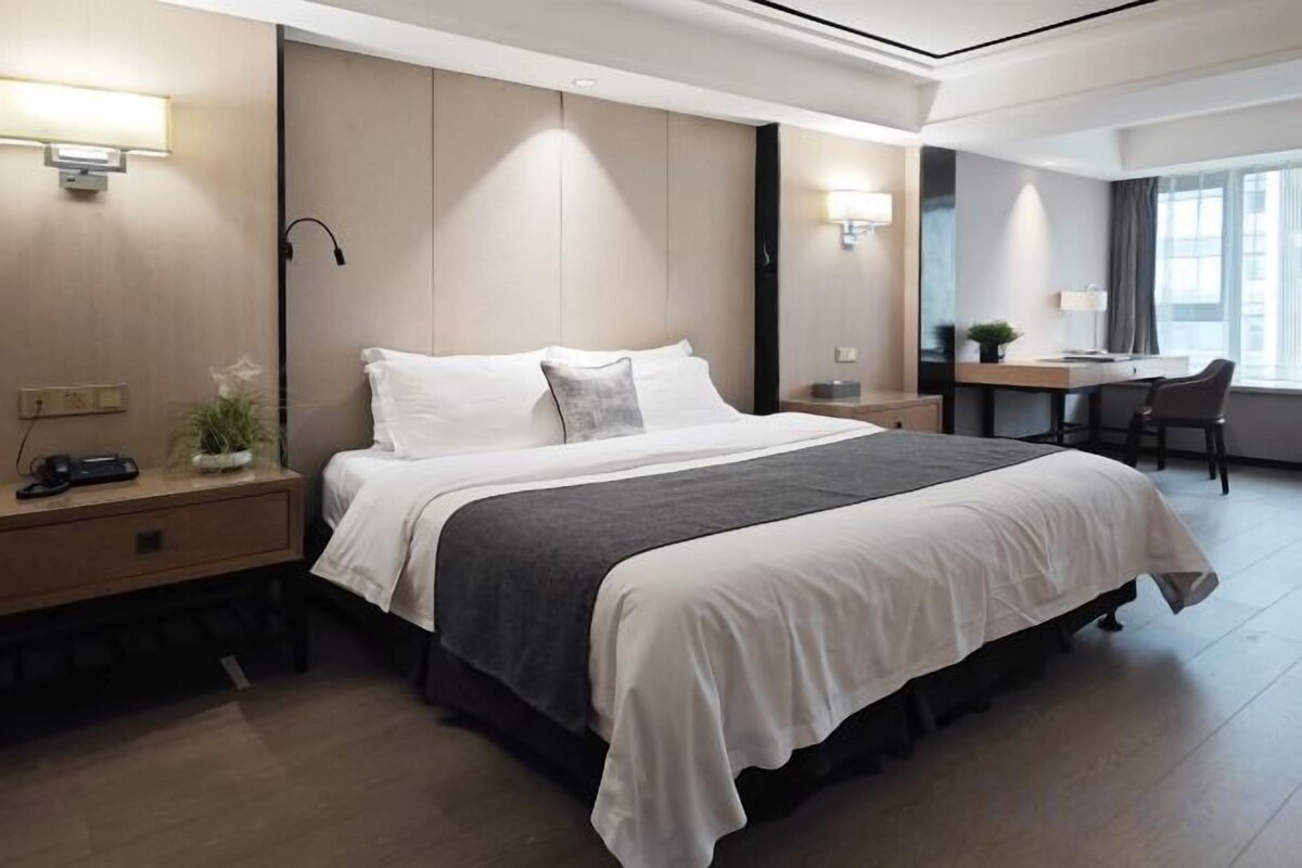 A modern hotel room with a large bed, bedside tables, a desk, and a chair.