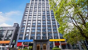 Ein mehrstöckiges Gebäude mit moderner Architektur, das einen zentralen Eingang mit Glasüren und eine umlaufende Grünanlage aufweist.
