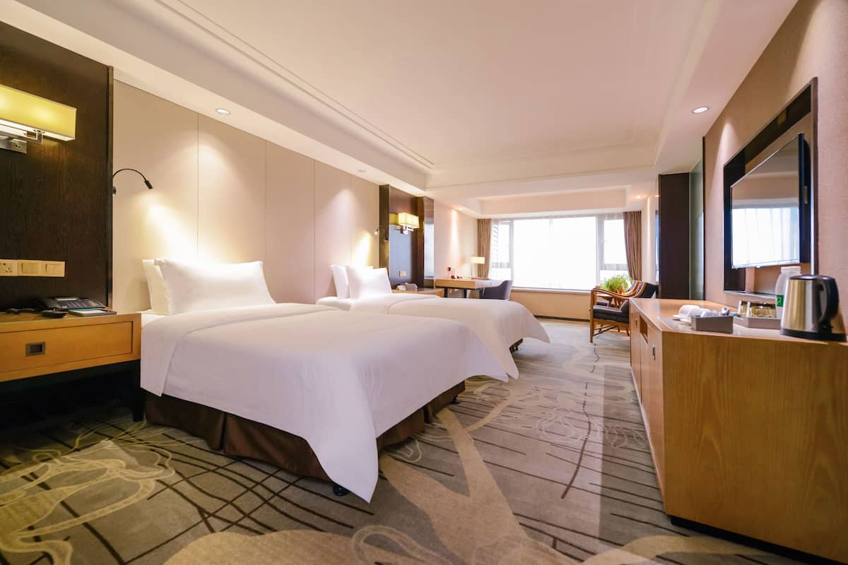A hotel room with two beds, a desk, a chair, a small table, and a large window.