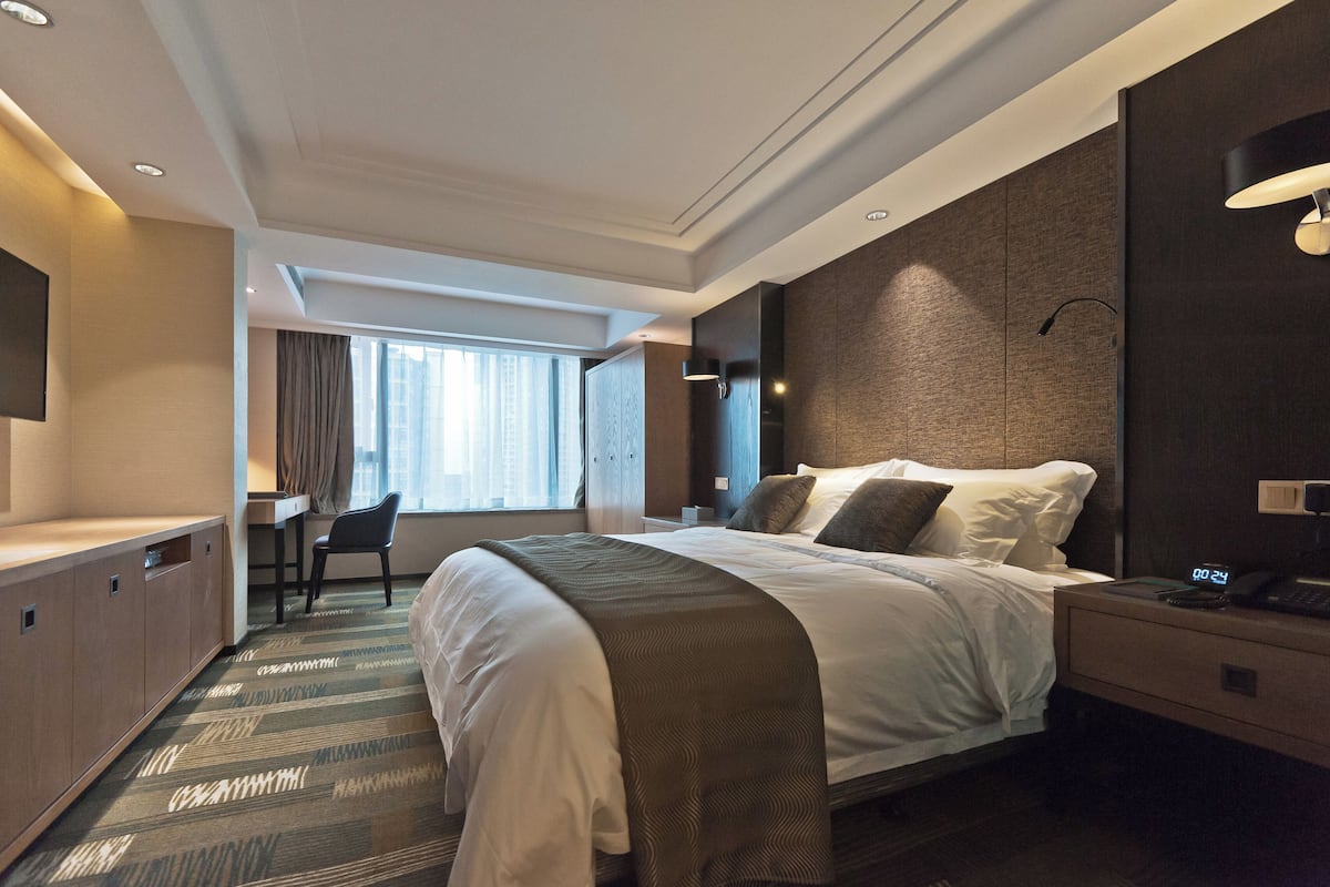 A modern hotel room with a large bed, a desk, and a chair.