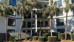 A multi-story building with balconies, palm trees, and a clear sky. - Spacious 2-suite Condo 5-Minute Walk to the Beach. (Hilton Head Island)